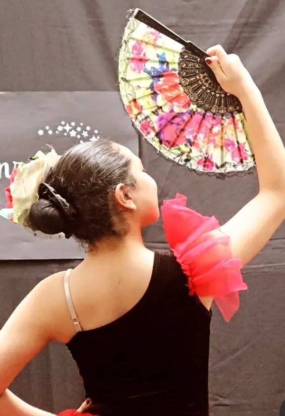 Luciana de espaldas, con un abanico floral en alto, durante una presentación de danza